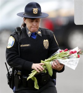 Newtown Police Officer Maryhelen McCarthy places flowers at a makeshift memorial outside St. Rose of Lima Roman Catholic Church, Sunday, Dec. 16, 2012, in Newtown, Conn. On Friday, a gunman allegedly killed his mother at their home and then opened fire inside the Sandy Hook Elementary School, killing 26 people. (AP Photo/Julio Cortez)