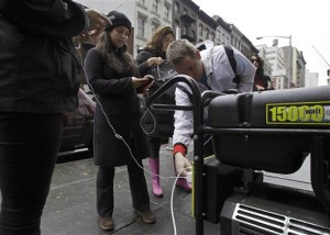 People in New York's Tribeca neighborhood, without power because of superstorm Sandy, wait for a chance to charge their mobile phones on an available generator setup on a sidewalk, Tuesday, Oct. 30, 2012. Sandy, the storm that made landfall Monday, caused multiple fatalities, halted mass transit and cut power to more than 6 million homes and businesses. (AP Photo/Richard Drew)