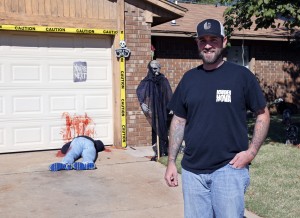 Johnnie Mullins poses with his controversial Halloween display featuring headless dummies dressed in his work clothes at his home in Mustang, Okla, Thursday, Oct. 17, 2013. In the display, one dummy lies along a blood-stained garage door with a sign reading "you're next" above it, and another, not shown, lies under a truck with blood splattered on the driveway. Mullins' wife, Jennifer, said she got the idea for the macabre scene from the social media site Pinterest. (AP Photo/Sue Ogrocki)